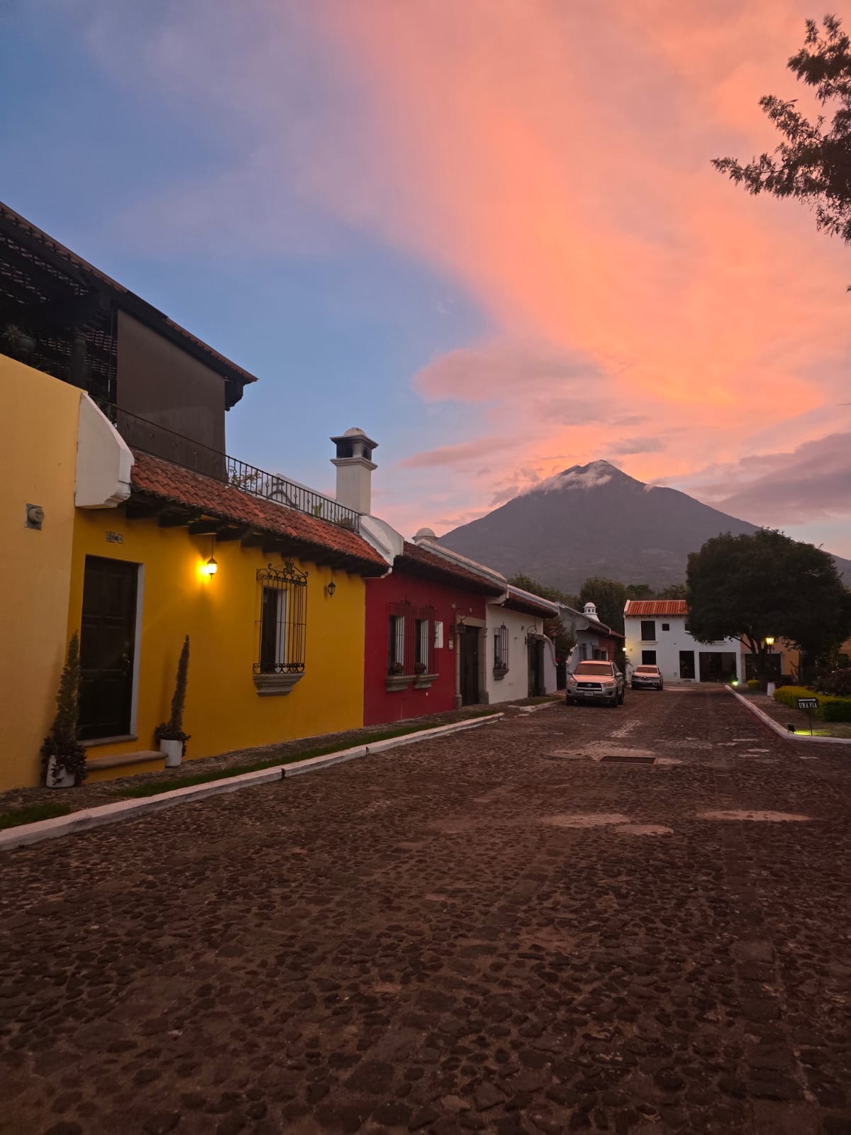 Around Condesa: colorful houses and a cobblestone street beneath a volcano and a pink sunset sky
